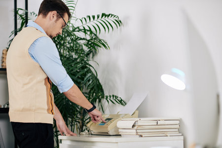 Young businessman in shirt and waistcoat receiving fax when working in office