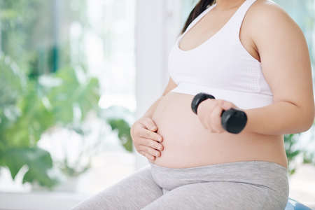 Cropped image of pregnant woman touching belly and doing exercise with small dumbbellの写真素材