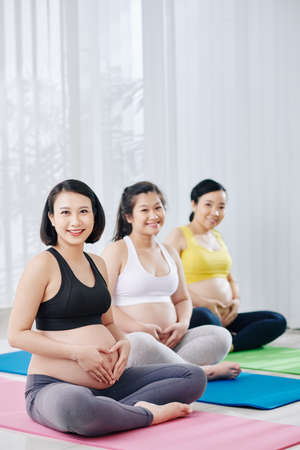 Happy smiling young Asian women sitting on yoga mat in sports class and making heart shape with their handsの写真素材