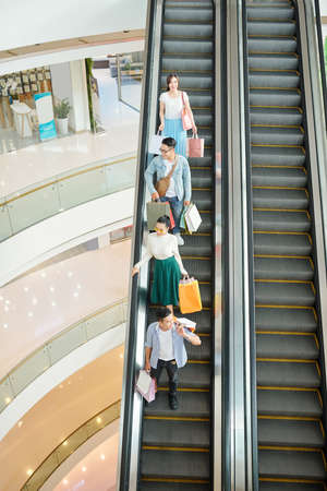 Young people with shopping bags standing on escalator in shopping mallの写真素材