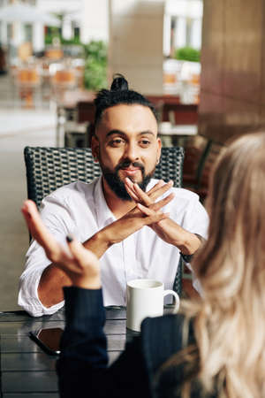 Smiling excited young entrepreneur listening to talking colleague at meeting in cafeの写真素材