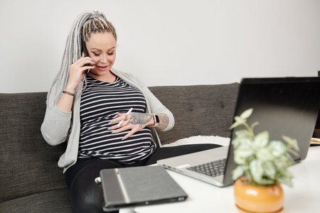 Pregnant woman taking on phone and touching belly feeling that baby is kicking