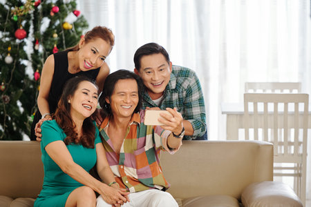 Group of jouful mature friends posing for selfie at Cheistmas tree at home
