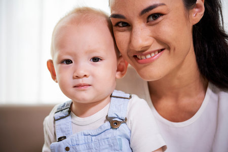 Portrait of happy smiling young mixed-race woman and hernewborn son looking at camera
