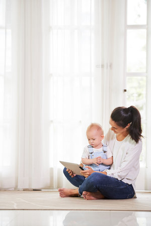 Young mom and her little child sitting on floor at home and watching animated film on digital tablet