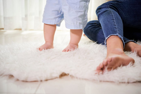 Cropped image of mother supporting little child walking on fur carpet at home