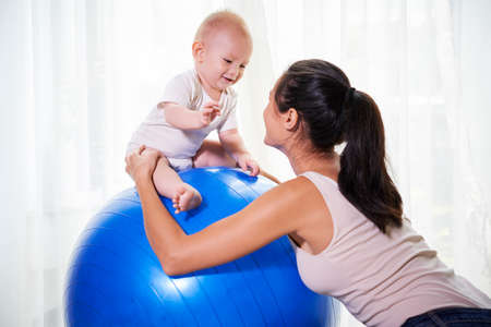 Fit young woman playing with smiling little kid sitting on fitness ballの写真素材