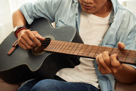 Cropped image of talented creative young man playing guitar at homeの写真素材