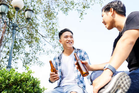 Two happy Asian men drinking beer and spending funny time together outdoorsの写真素材