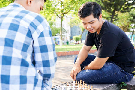 Two Asian guys sitting on bench on the street and playing chess togetherの写真素材