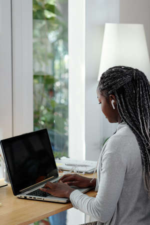 Pretty young female university student working on laptop at her desk at homeの写真素材