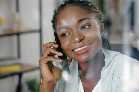 Portrait of happy young Black woman with white toothy smile talking on phone with colleague