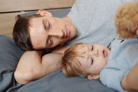 Young father lying on bed and resting together with his little son during sleep hourの写真素材