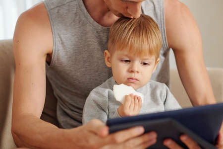 Little boy watching cartoons on digital tablet while sitting together with his fatherの写真素材