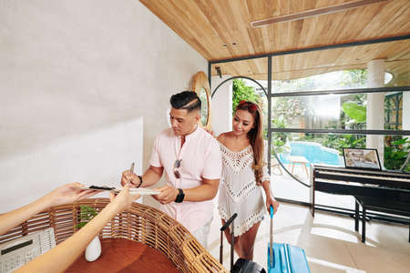 Man filling document for him and his wife when standing at reception of spa hotelの写真素材