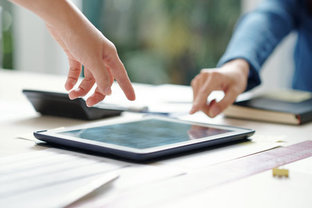 Close-up image of young entrepreneurs pointing at screen of digital tablet with report on office...