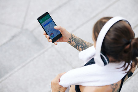 Fit young woman with towel trekking her activity via application on smartphone, view from above