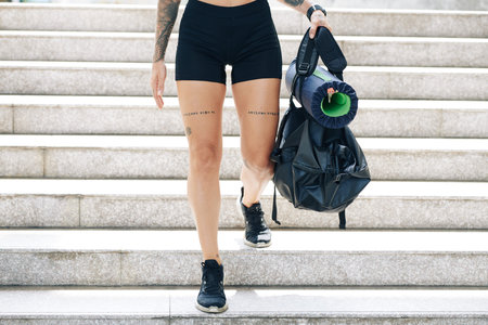 Cropped image of fit young woman in gym shorts walking down the stairs with gym bag in hands
