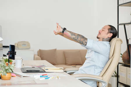 Mixed-race graphic designer stretching in his armchair after finishing work on big projectの写真素材