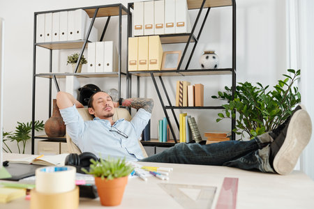 Graphic designer sleeping in his chair when enjoying short break after finishing work on big projectの写真素材