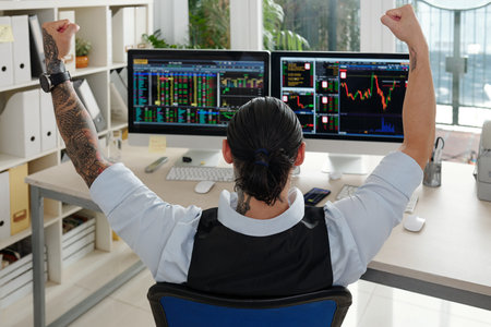 Excited male trader with ponytail raising hands when celebrating companies stock price increased, view from the backの写真素材