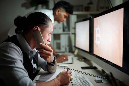 Serious trader talking on phone with client when looking at bitcoin price chart watch for trading opportunitiesの写真素材