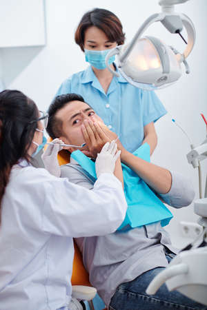 Dentist and nurse trying to reassure nervous patient scared of dental treatmentの写真素材