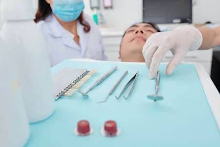 Dentist in silicone glove taking metal tools from tray when examining teeth of patientsの写真素材