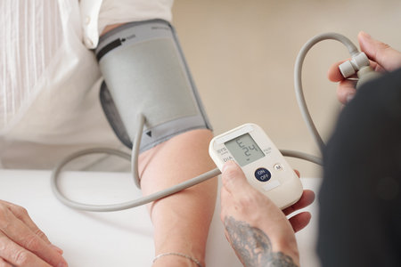 Close-up image of caring adult son healping senior mother to measure with electronic tonometer