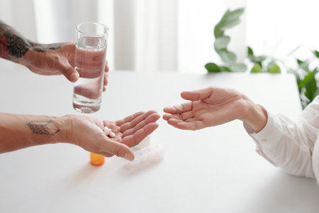 Hands of man giving glass of water and pills or supplements to his senior motherの写真素材