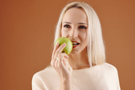 Pensive pretty young woman biting juicy green apple
