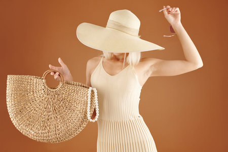 Beautiful woman in cream dress and straw hat holding wicker bag and sunglassesの写真素材