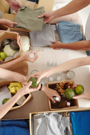 Hands of volunteers packing food, waterr and clothes in packages for people in need, view from aboveの写真素材