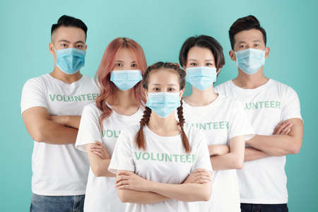 Team of young Vietnamese volunteers in protective masks standing behind their female leaderの写真素材