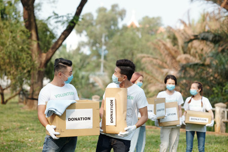 Volunteers carrying boxes with clothes donated by people during event in local park