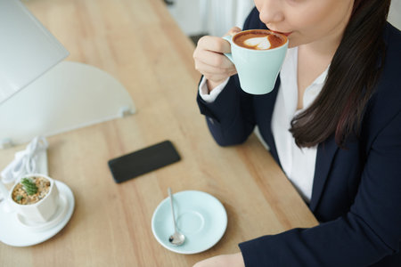 Cropped image of young businesswoman drinking cup of latte at cafe table