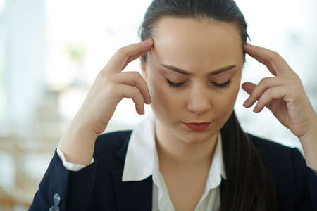 Pretty young female entrepreneur suffering from severe headache or migraine after working all dayの写真素材