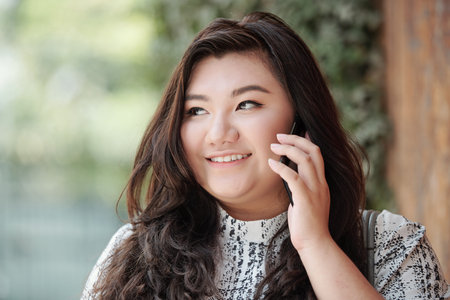 Face of beautiful smiling young mixed-race woman standing outdoors and talking on phoneの写真素材