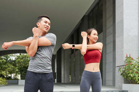 Positive young Asian couple stretching arms after jogging outdoorsの写真素材