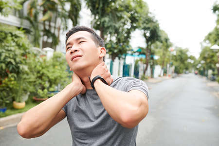 Young Asian sportsman suffering from pain in his neck, he is massaging neck to get reliefの写真素材