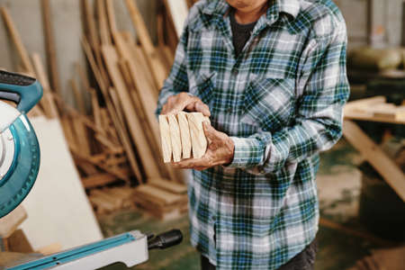 Cropped image of senior carpenter holding freshly cut wooden blocks he prepared for furniture itemの写真素材