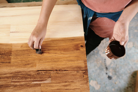 Hands of carpenter covering wood board with lacquer to protect it and give shineの写真素材