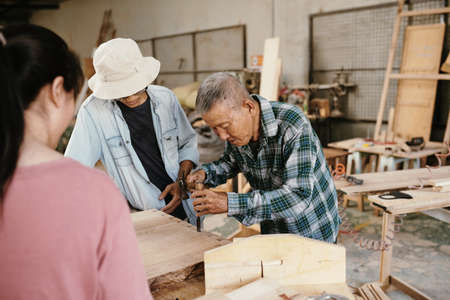 Senior experienced Vietnamese carpenter showing his grandchildren how to use chisel and hammer when working with woodの写真素材