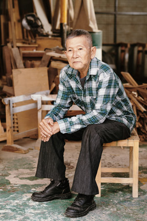 Contemplating senior Vietnamese carpenter sitting on stool in his workshopの写真素材