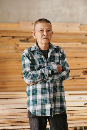 Portrait of serious senior Vietnamese carpenter in plaid shirt crossing arms and looking at cameraの写真素材