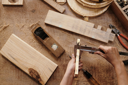 Hands of carpenter measuring wooden planks with vernier caliper, view from aboveの写真素材