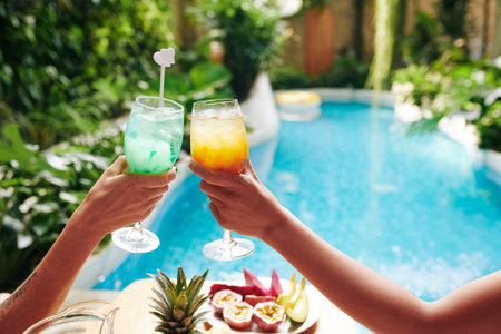 Hands of young women relaxing by swimming pool and drinking ice cold sweet fruit cocktailsの写真素材