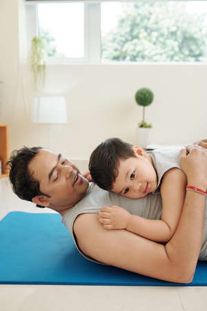 Father and little son resting on the floor after working out together at homeの写真素材