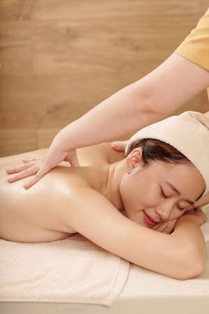 Smiling young woman having beauty day, she is getting professional back massage in spa salonの写真素材