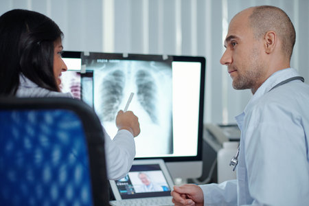 Team of pulmonologists discussing chest and lungs x-ray of patient with coronavirus on computer...